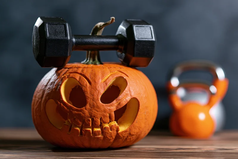 Carved halloween pumpkin with dumbbell balanced on top on wooden table