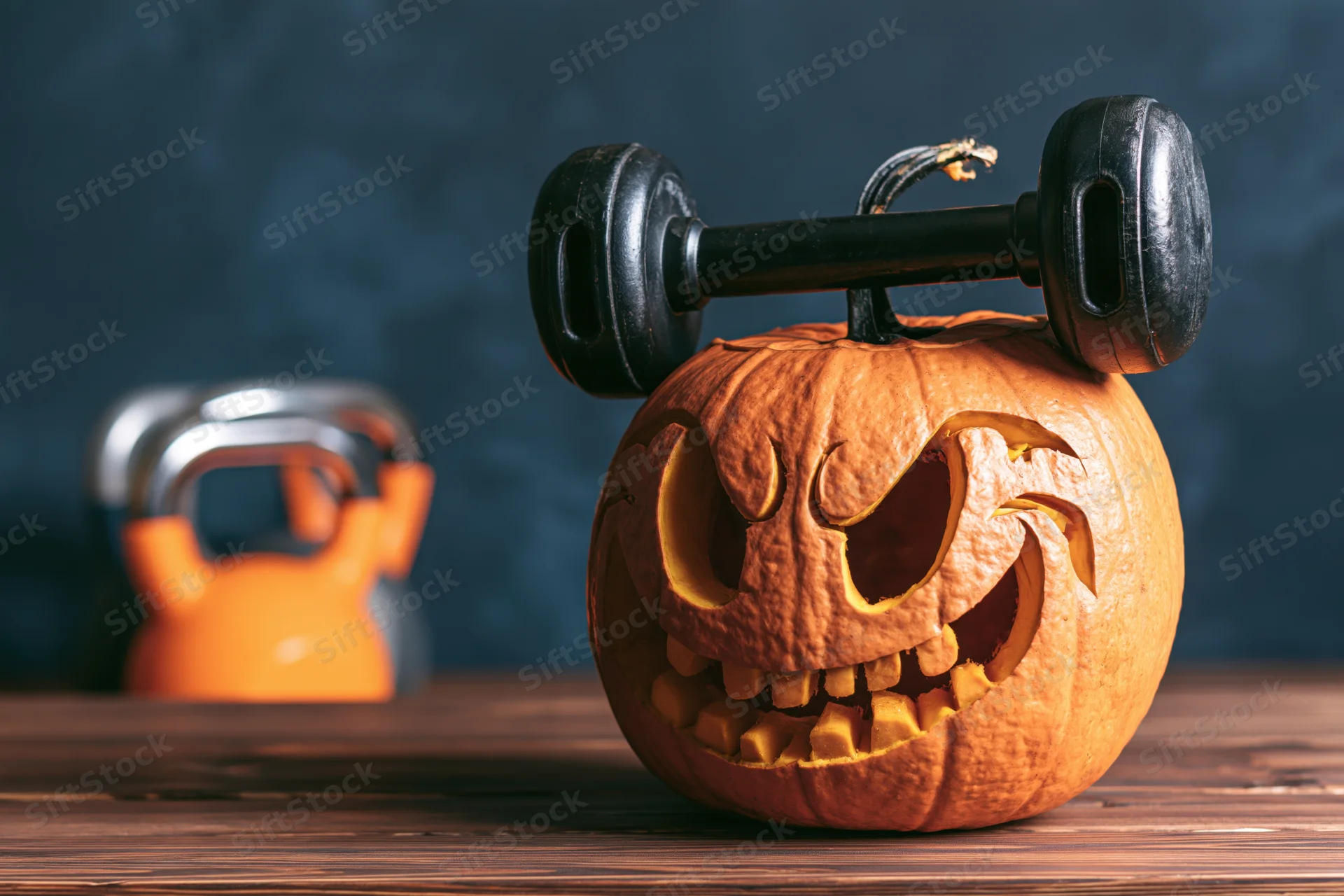 Carved halloween pumpkin with dumbbell balanced on top on wooden table