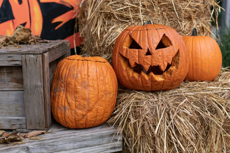 Carved jack-o-lantern with jagged grin resting on hay bales beside a wooden crate