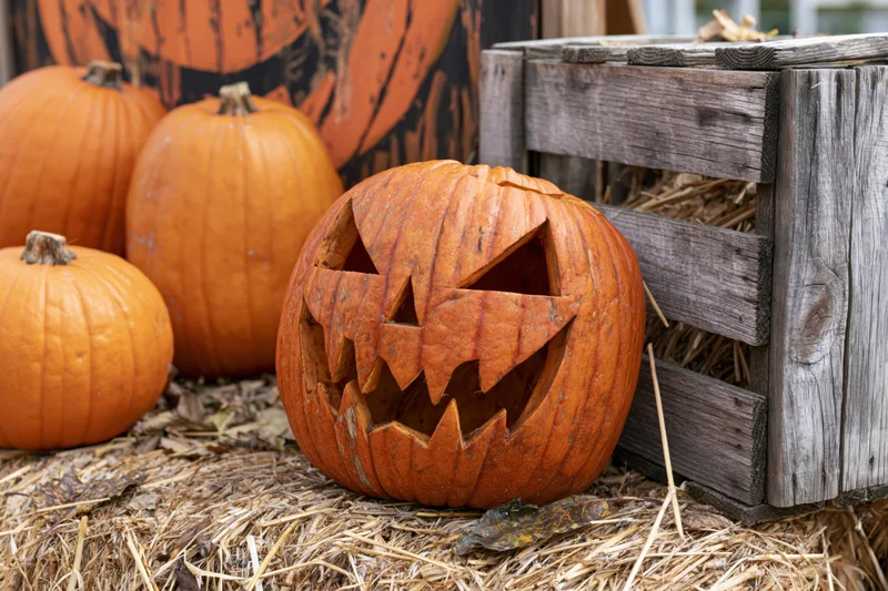 Carved jack-o-lantern with jagged grinning face resting on hay beside a wooden crate