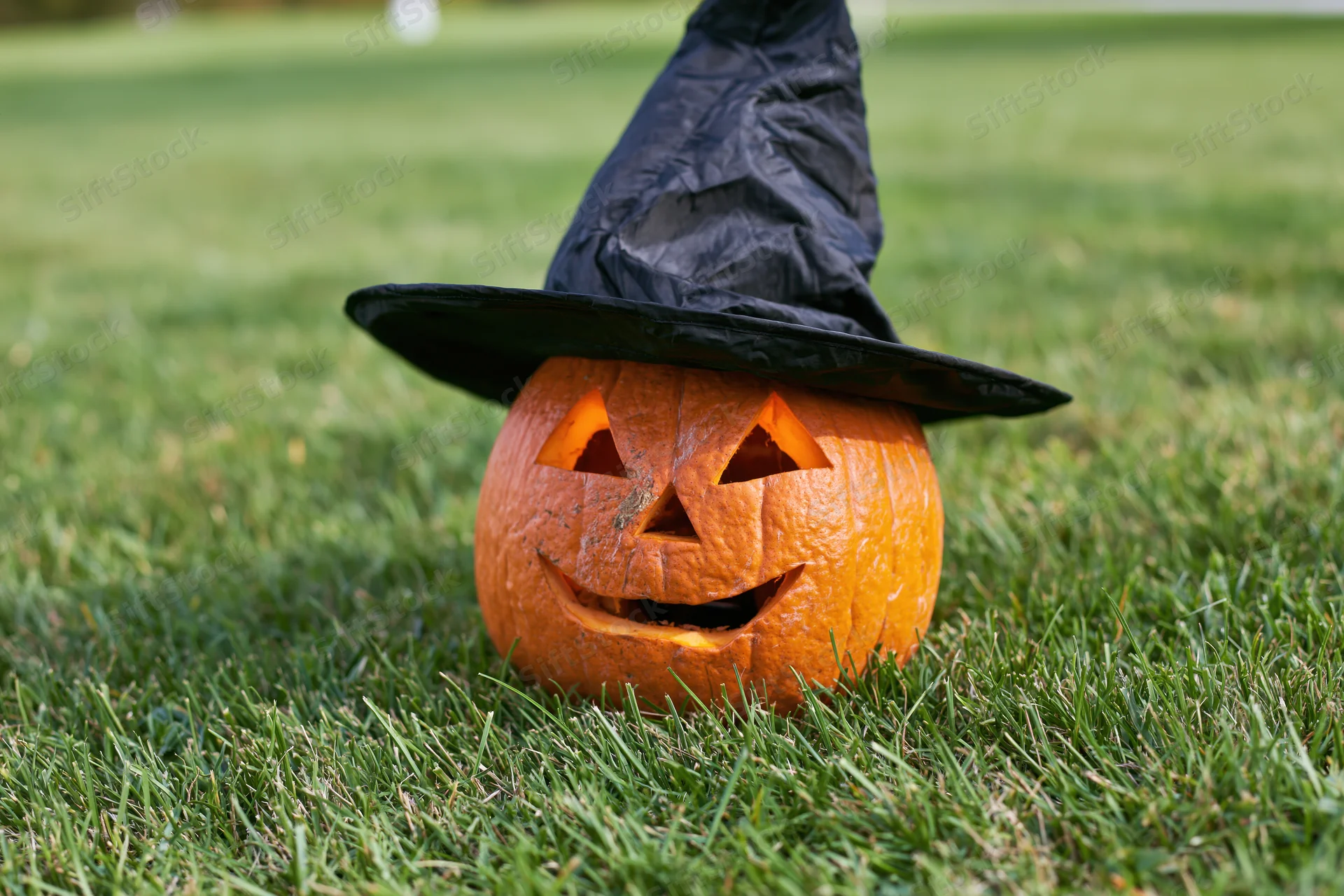 Carved jack-o-lantern with smiling face wearing witch hat on grass