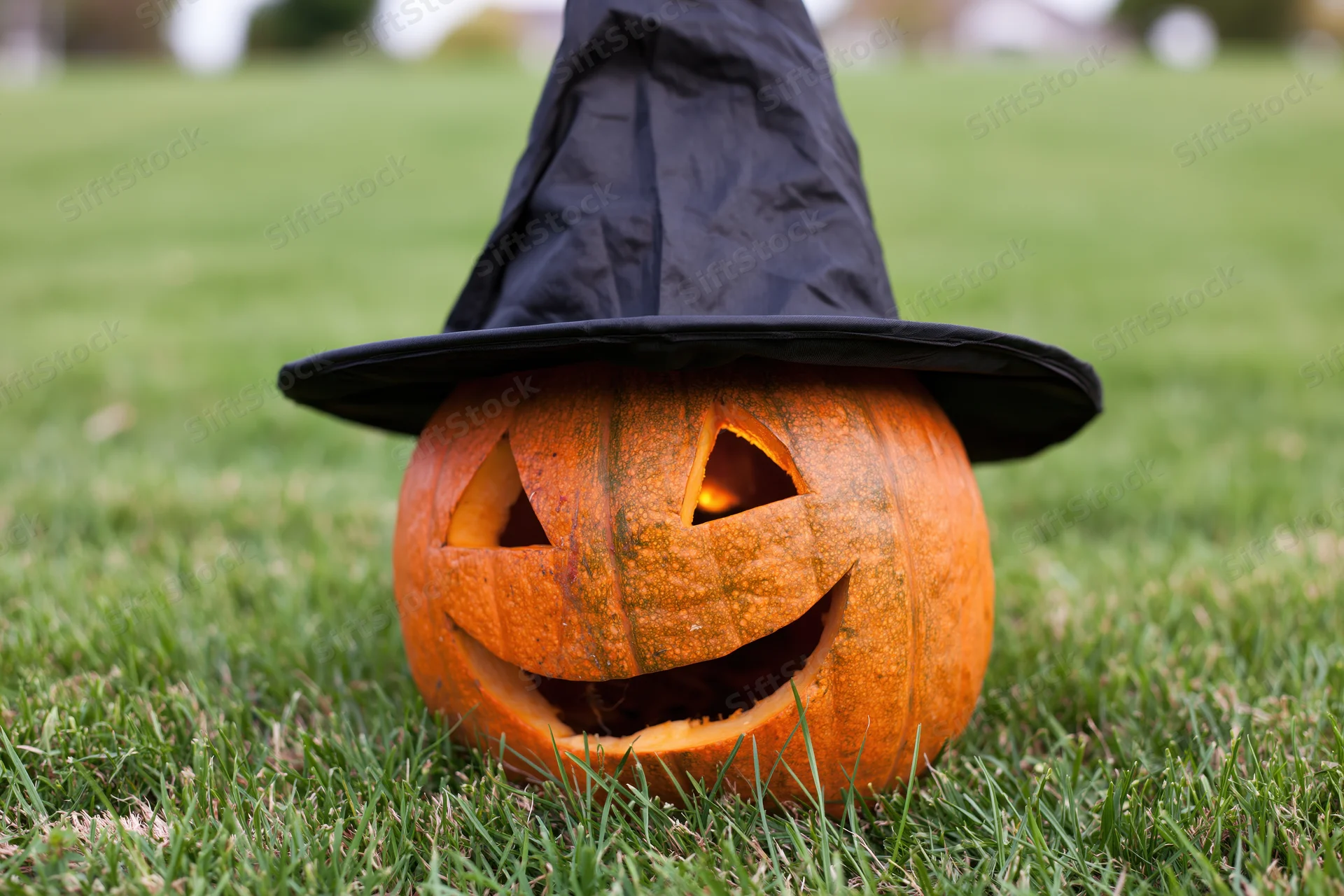 Carved jack-o-lantern with smiling face wearing witch hat on grass lawn