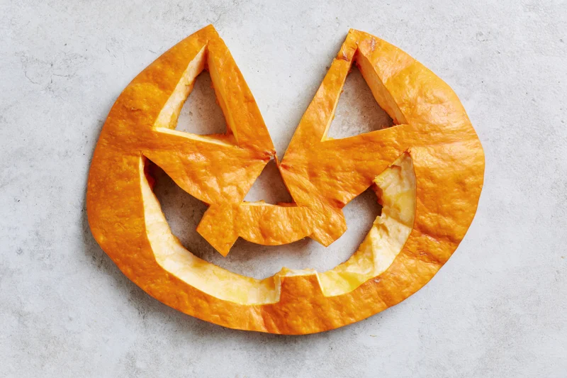 Carved pumpkin face pieces arranged flat on a light grey concrete surface