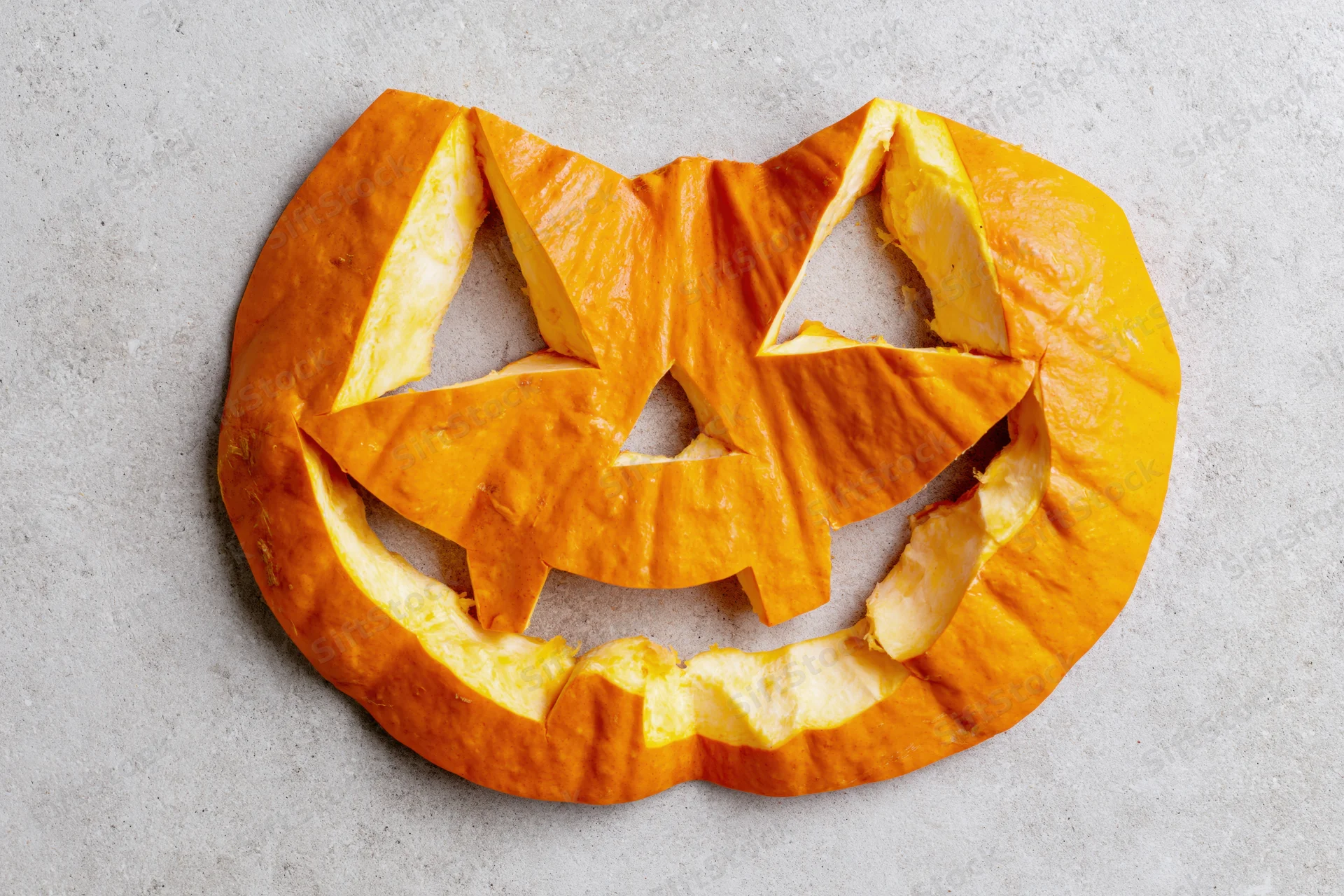 Carved pumpkin face pieces arranged flat on a light grey concrete surface
