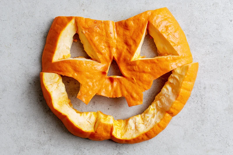 Carved pumpkin face pieces arranged flat on a light grey concrete surface