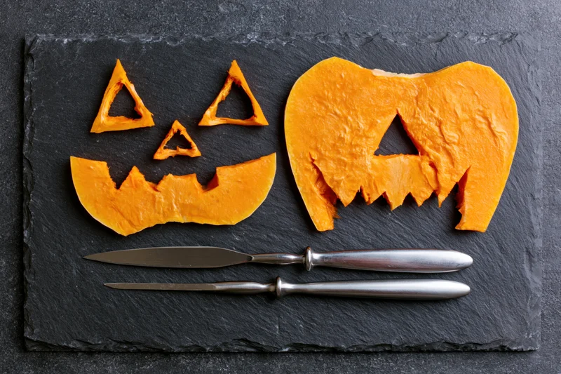 Carved pumpkin face pieces arranged on dark slate with carving knives