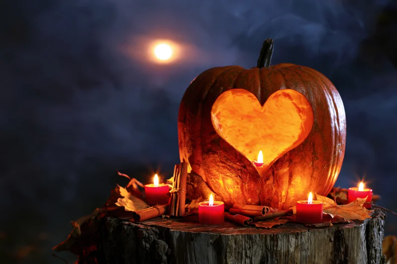 Carved pumpkin with heart design illuminated by candles on a wooden stump at night