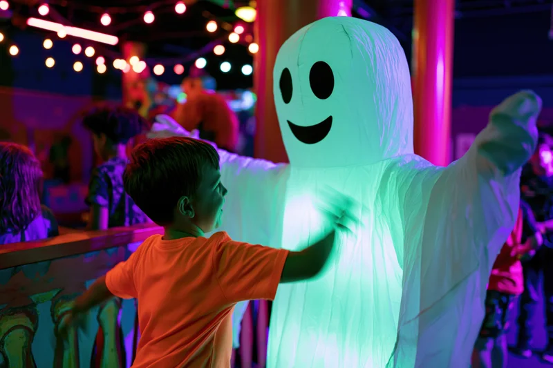 Young boy in orange shirt reaching toward glowing inflatable ghost at halloween party