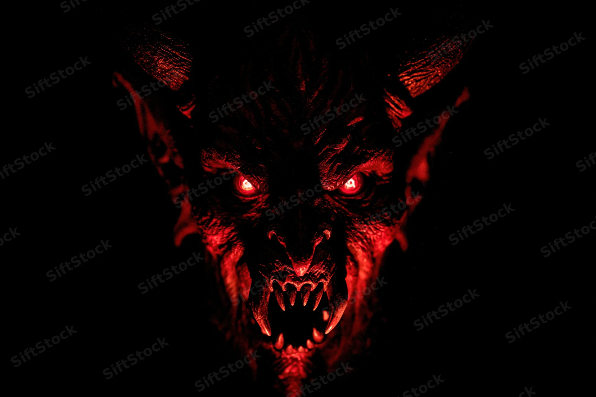 Close-up of a demonic latex mask with glowing red eyes and sharp teeth against a dark background