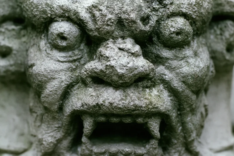 Close-up of a weathered stone gargoyle face with open mouth and fanged teeth on a building facade