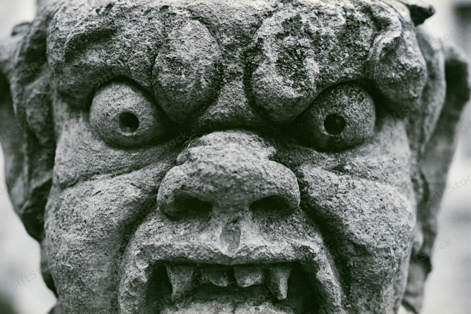Close-up of a weathered stone gargoyle face with fanged mouth and bulging eyes