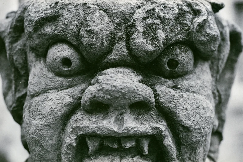 Close-up of a weathered stone gargoyle face with fanged mouth and bulging eyes