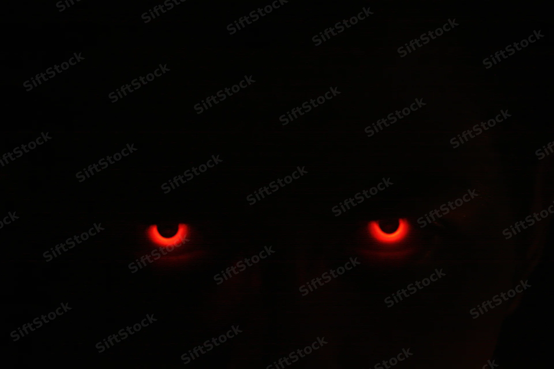 Glowing red eyes staring from complete darkness