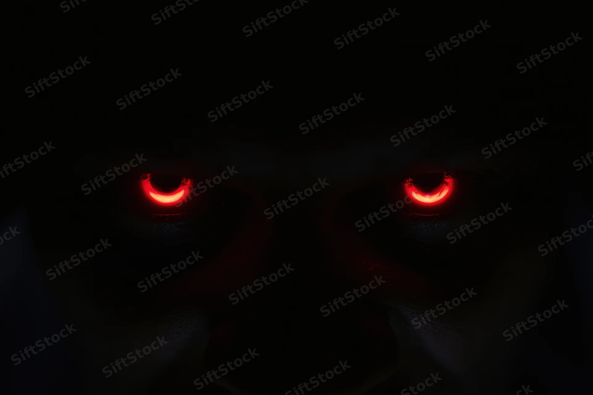 Glowing red eyes staring from complete darkness