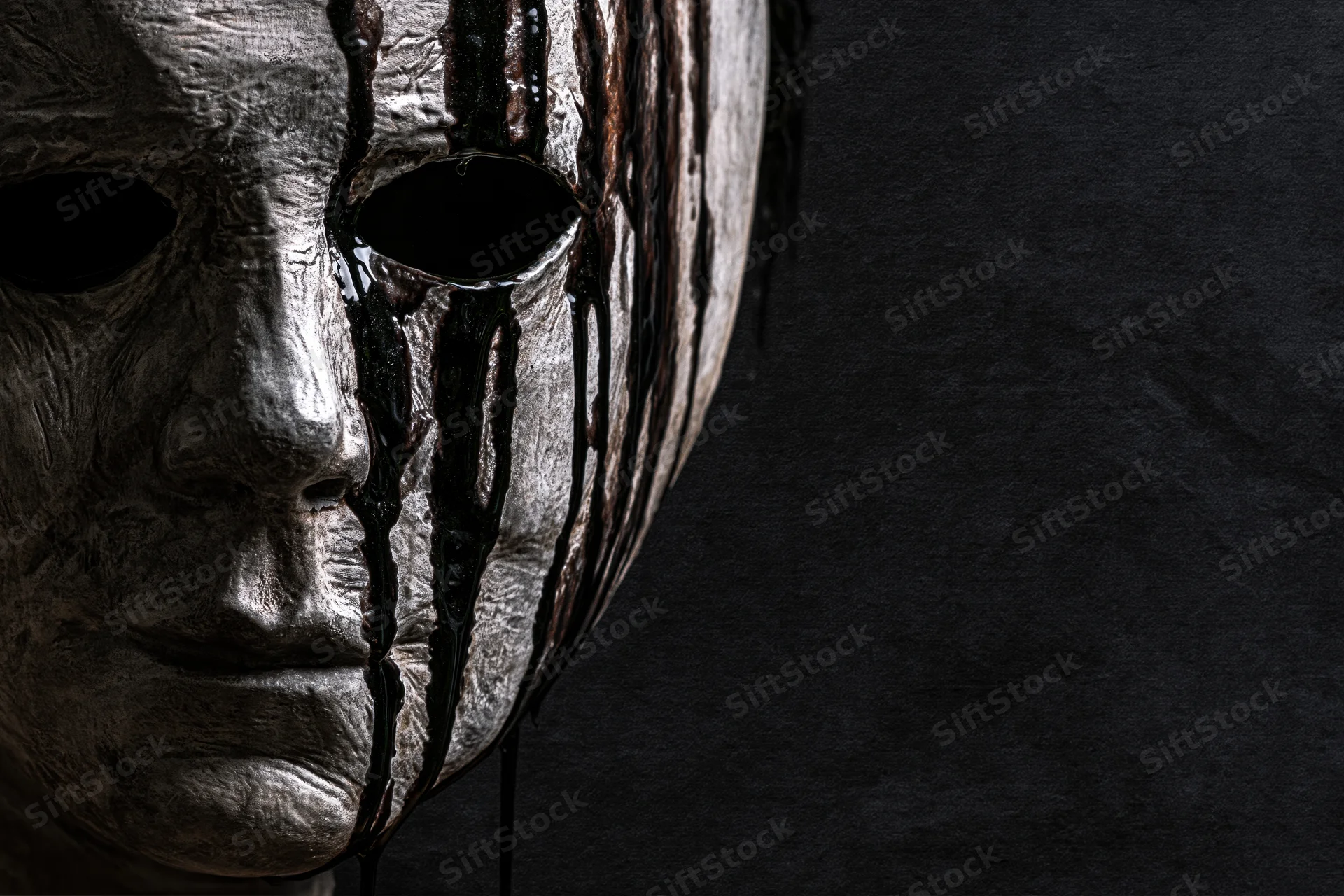 Close-up side profile of a weathered horror mask with blood dripping down its surface against a dark background