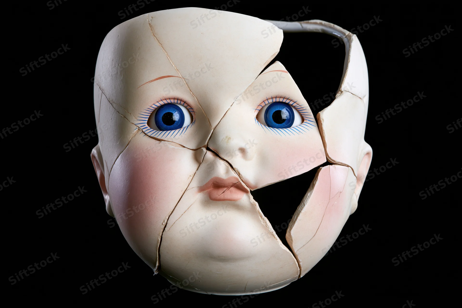 Cracked porcelain doll head with blue glass eyes against black background