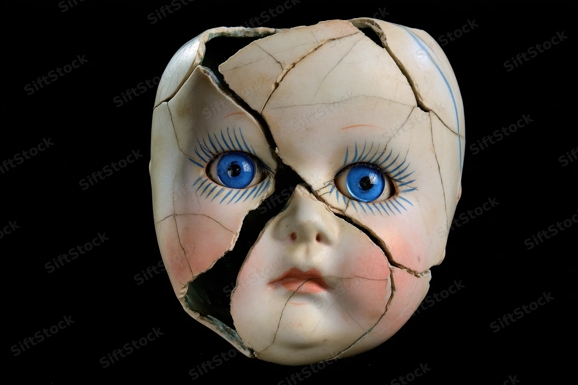 Cracked porcelain doll head with blue glass eyes on black background