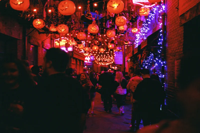Crowd walking through a narrow urban street decorated with glowing pumpkin lanterns at night