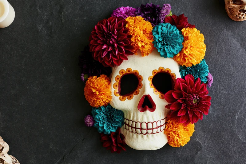 Sugar skull mask decorated with marigolds and colorful flowers on dark stone surface