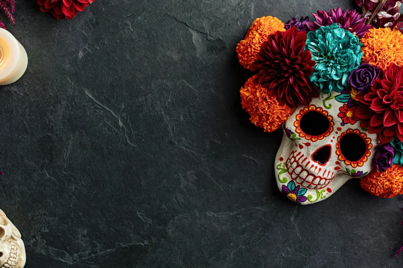 Decorated sugar skull mask with marigolds on dark stone surface