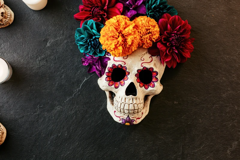 Painted sugar skull decorated with marigolds and colorful flowers on dark stone surface