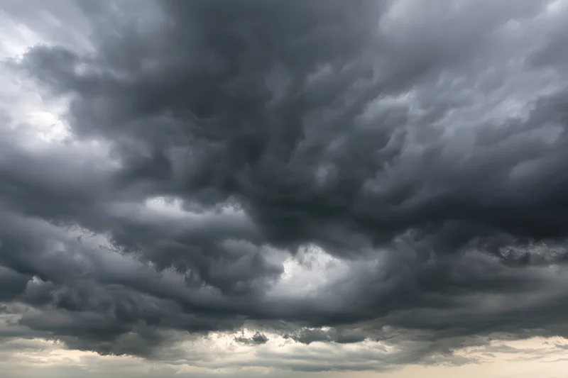 Dark storm clouds filling the sky with swirling cumulonimbus formations and breaks of light at the horizon