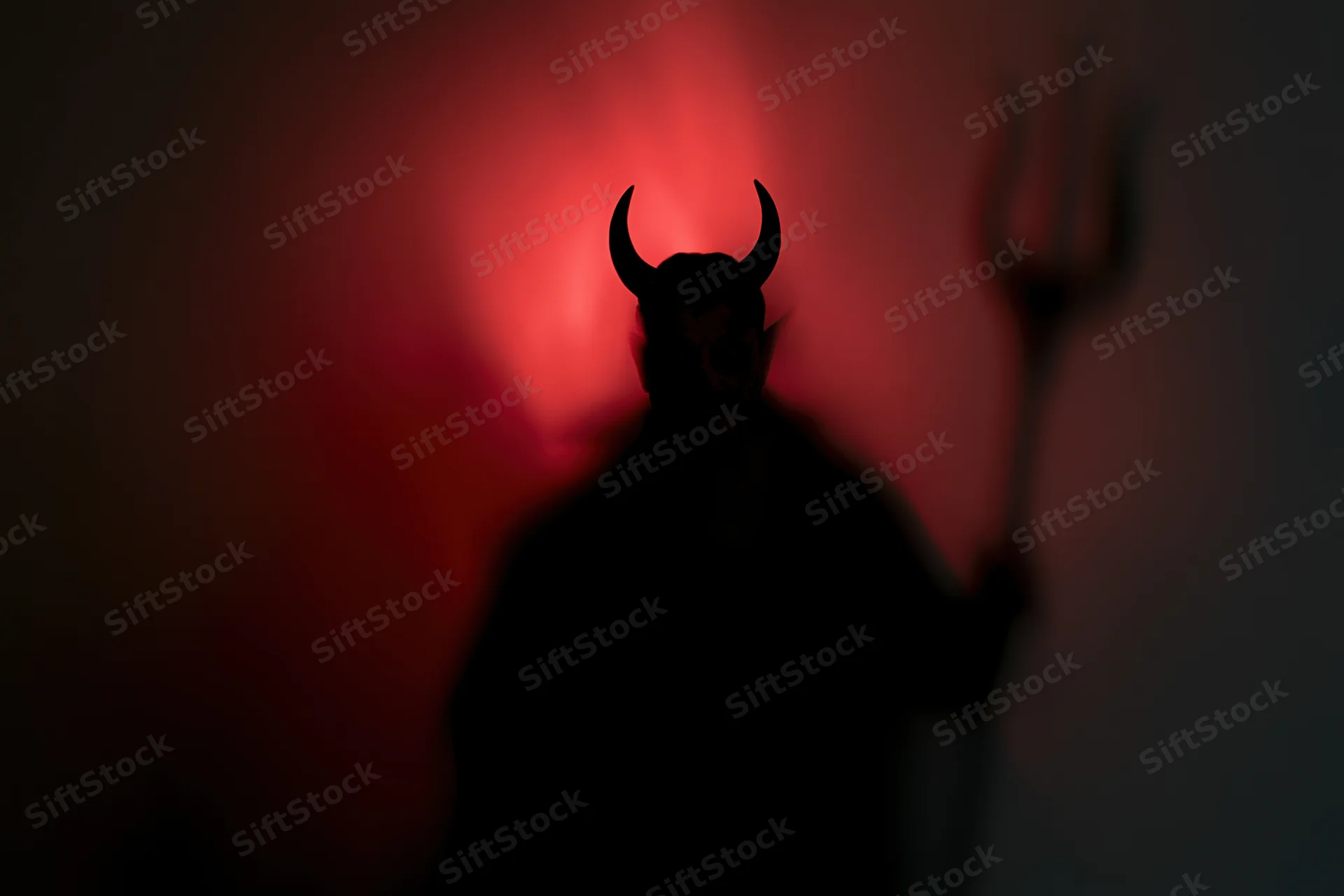 Silhouette of a devil figure with horns holding a trident against red glowing background