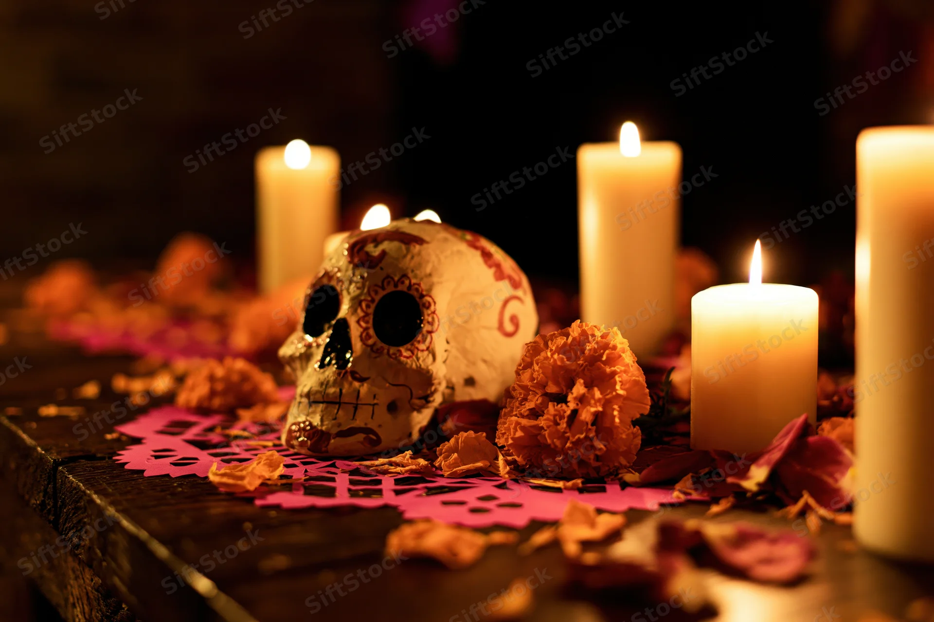 Decorated altar with painted skull, lit candles, marigolds and papel picado on dark wooden surface
