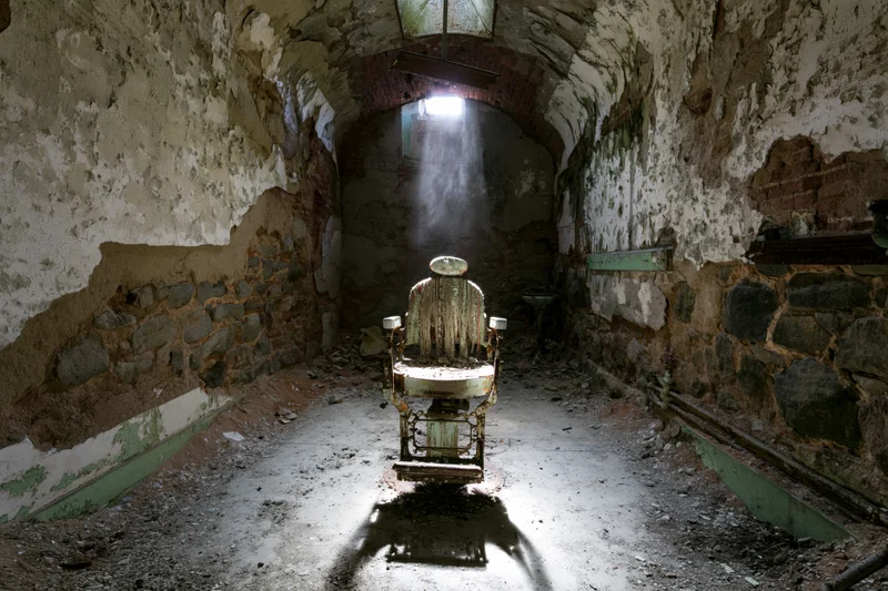 Decayed vintage dental chair centered in a crumbling stone corridor with light beam from above