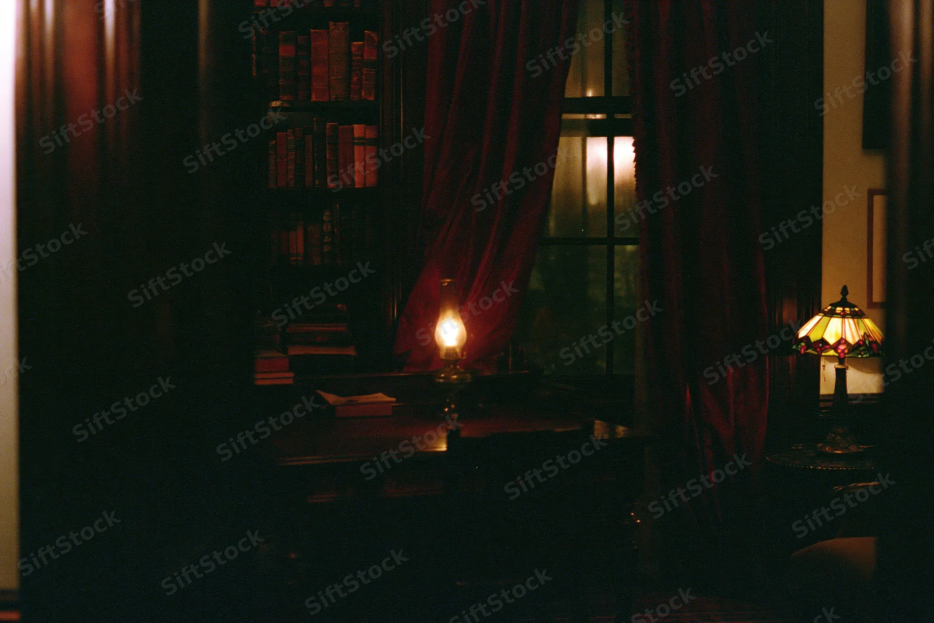 Dimly lit vintage study room with dark wood desk, bookshelf, and lamps at night