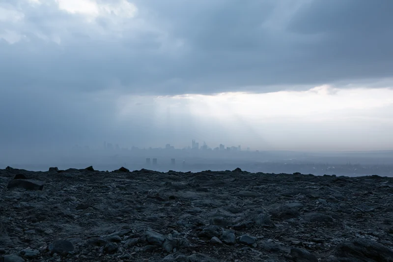 Distant city skyline seen through storm haze from rocky foreground