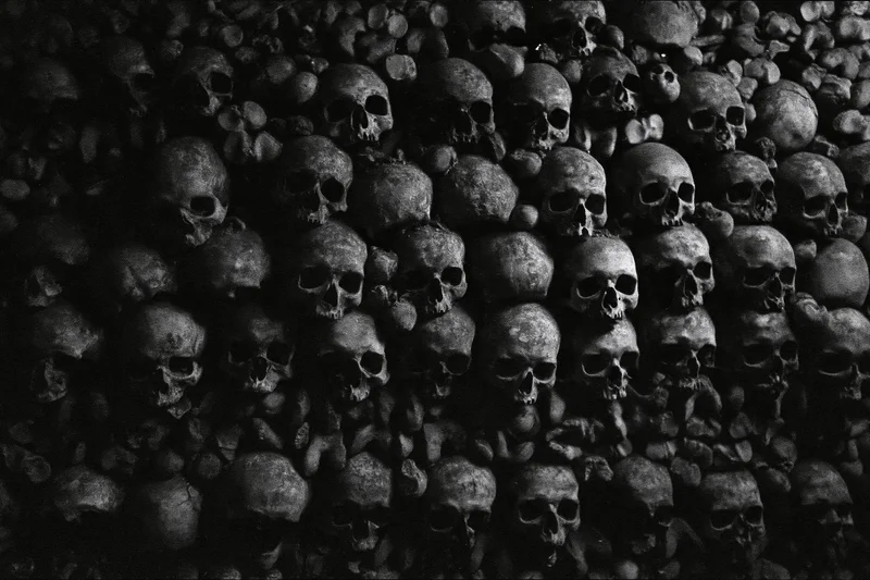 Ancient human skulls and bones densely packed on a dark floor in an ossuary