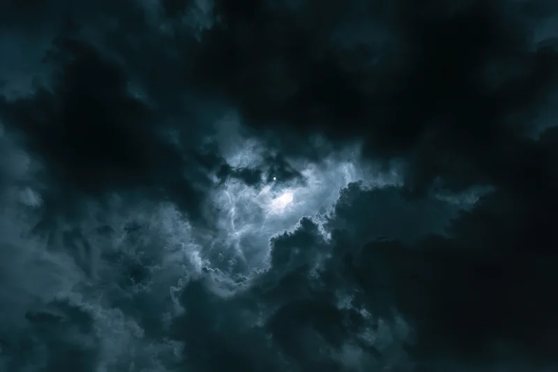 Stormy night sky filled with dark clouds and a glowing moonlight break