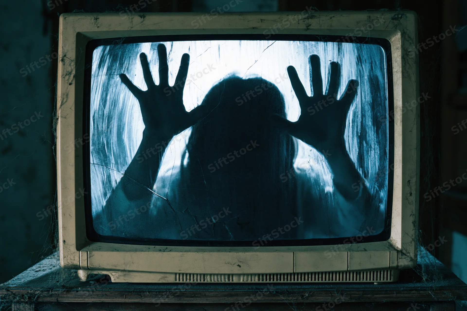 Silhouette of a ghostly figure with hands pressed against the screen of a dusty vintage crt television on a wooden table