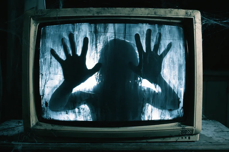 Shadowy figure with hands pressed against dusty vintage crt television screen in dark room