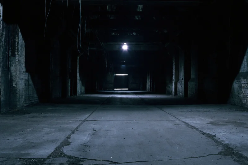 Empty abandoned industrial warehouse interior with cracked concrete floor and dim overhead lighting