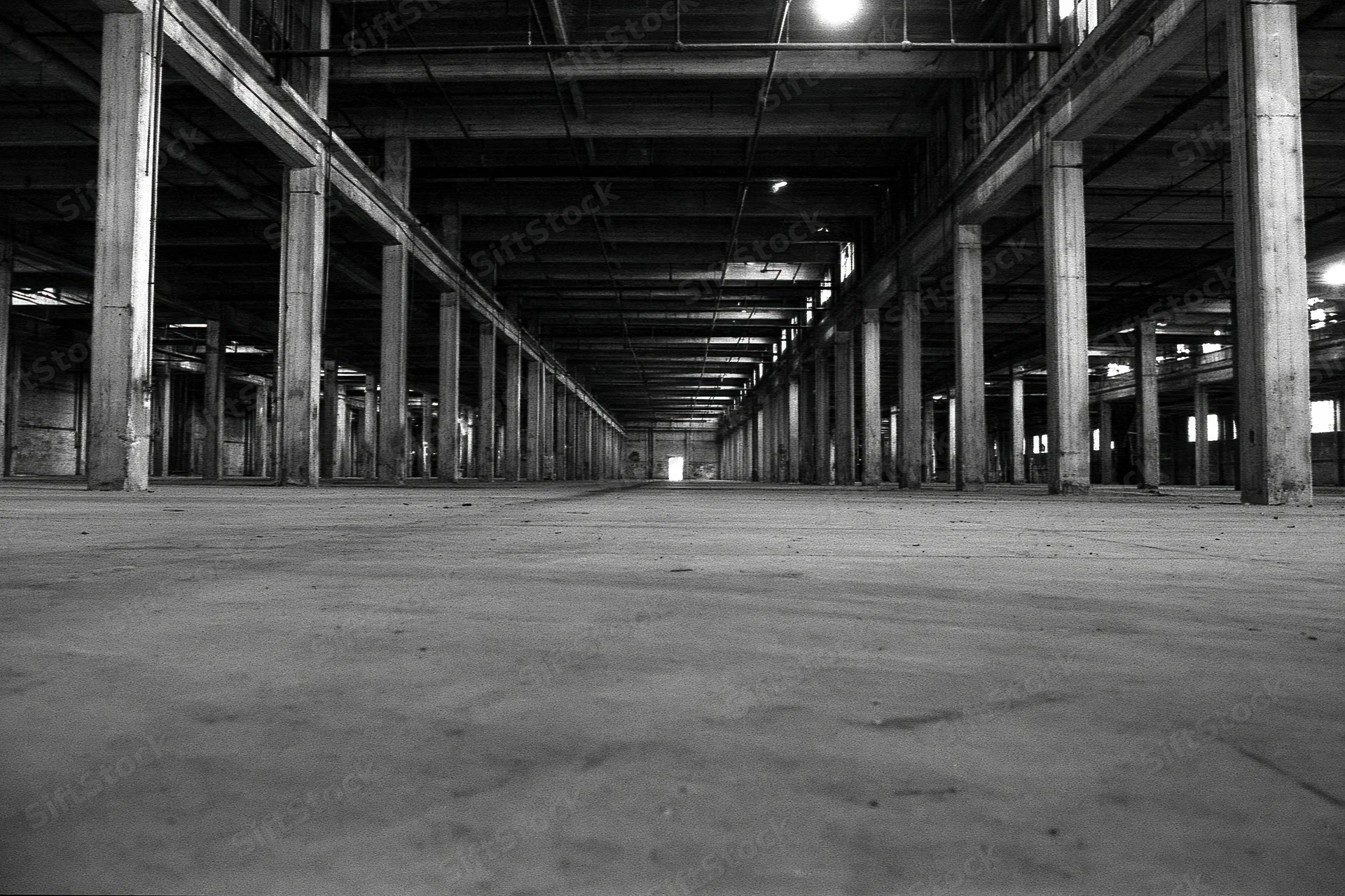 Empty abandoned industrial warehouse interior with concrete floor and rows of pillars under exposed ceiling beams