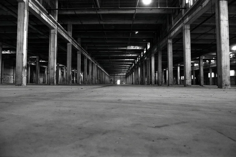 Empty abandoned industrial warehouse interior with concrete floor and rows of pillars under exposed ceiling beams