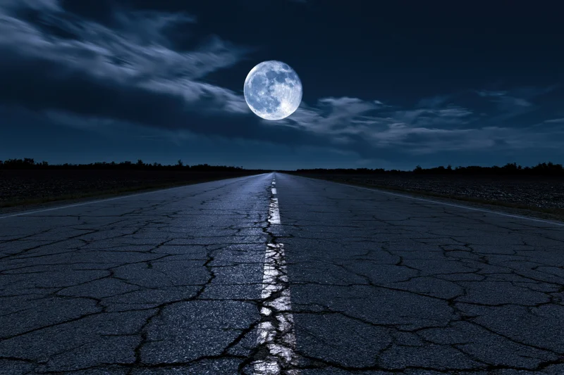 Cracked asphalt road stretching to the horizon under a full moon at night