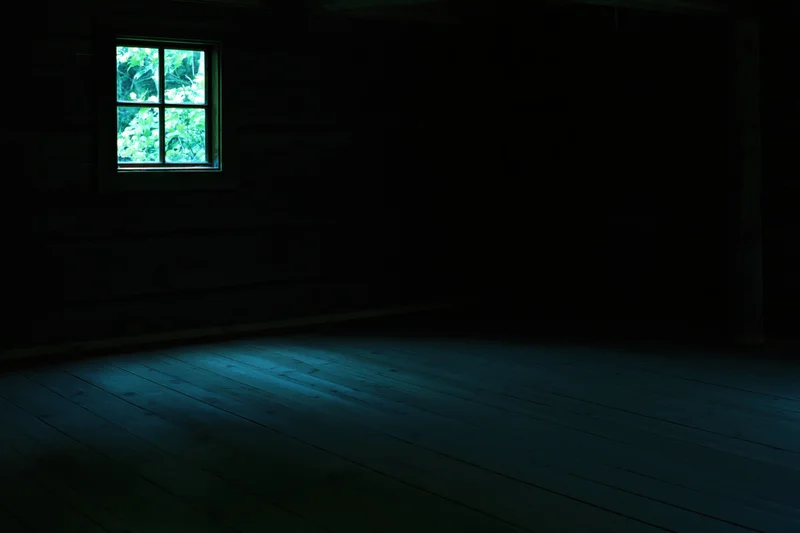 Dark empty wooden room with small four-pane window showing green foliage outside