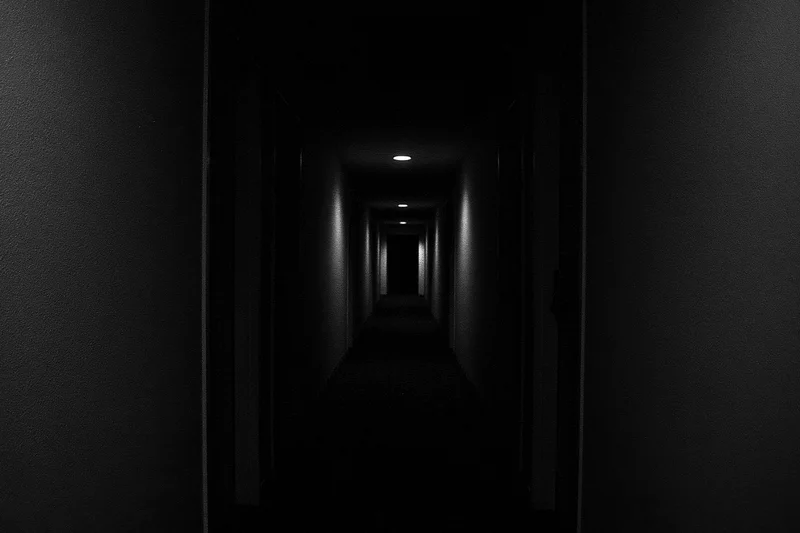 Dark hotel corridor receding into shadow with recessed ceiling lights and textured walls