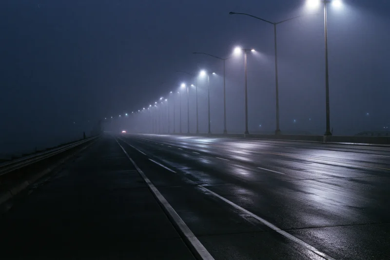 Empty multi-lane highway at night shrouded in dense fog with wet pavement and streetlights glowing through mist