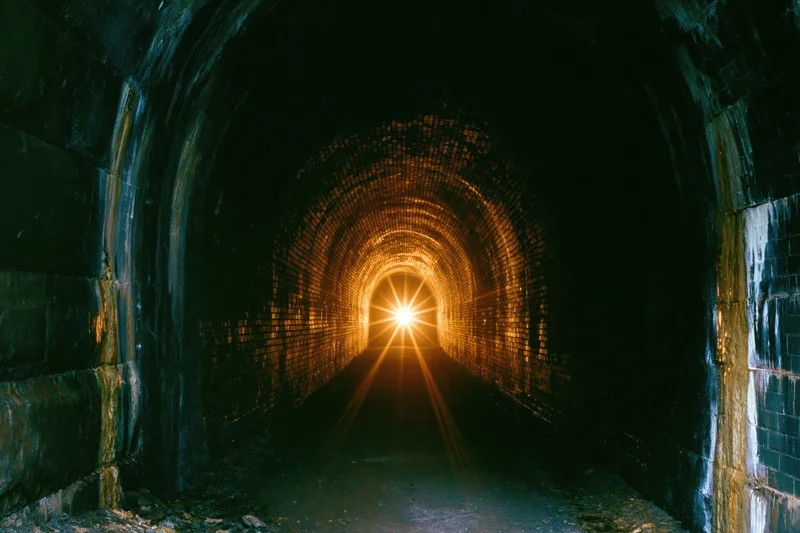 View down an old brick tunnel toward a bright light at the end