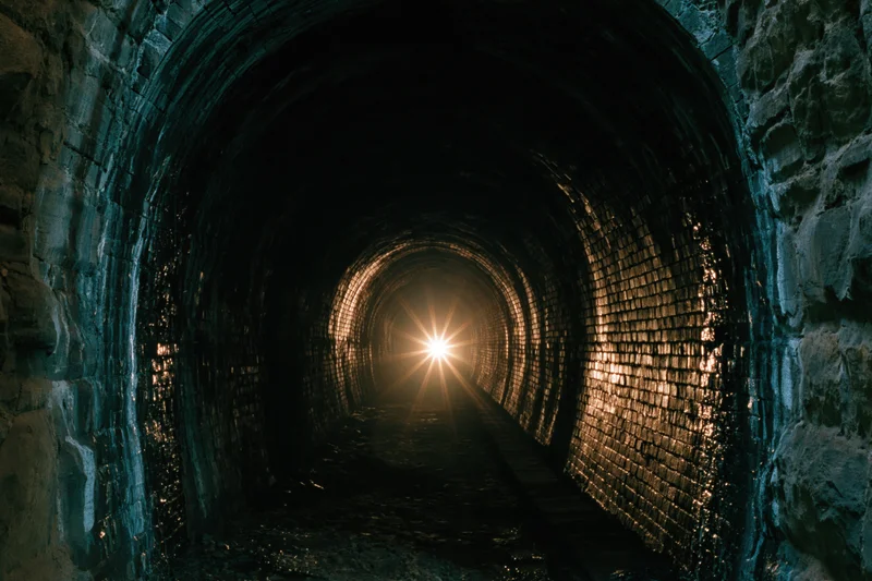 View down an old brick tunnel toward a bright light at the end