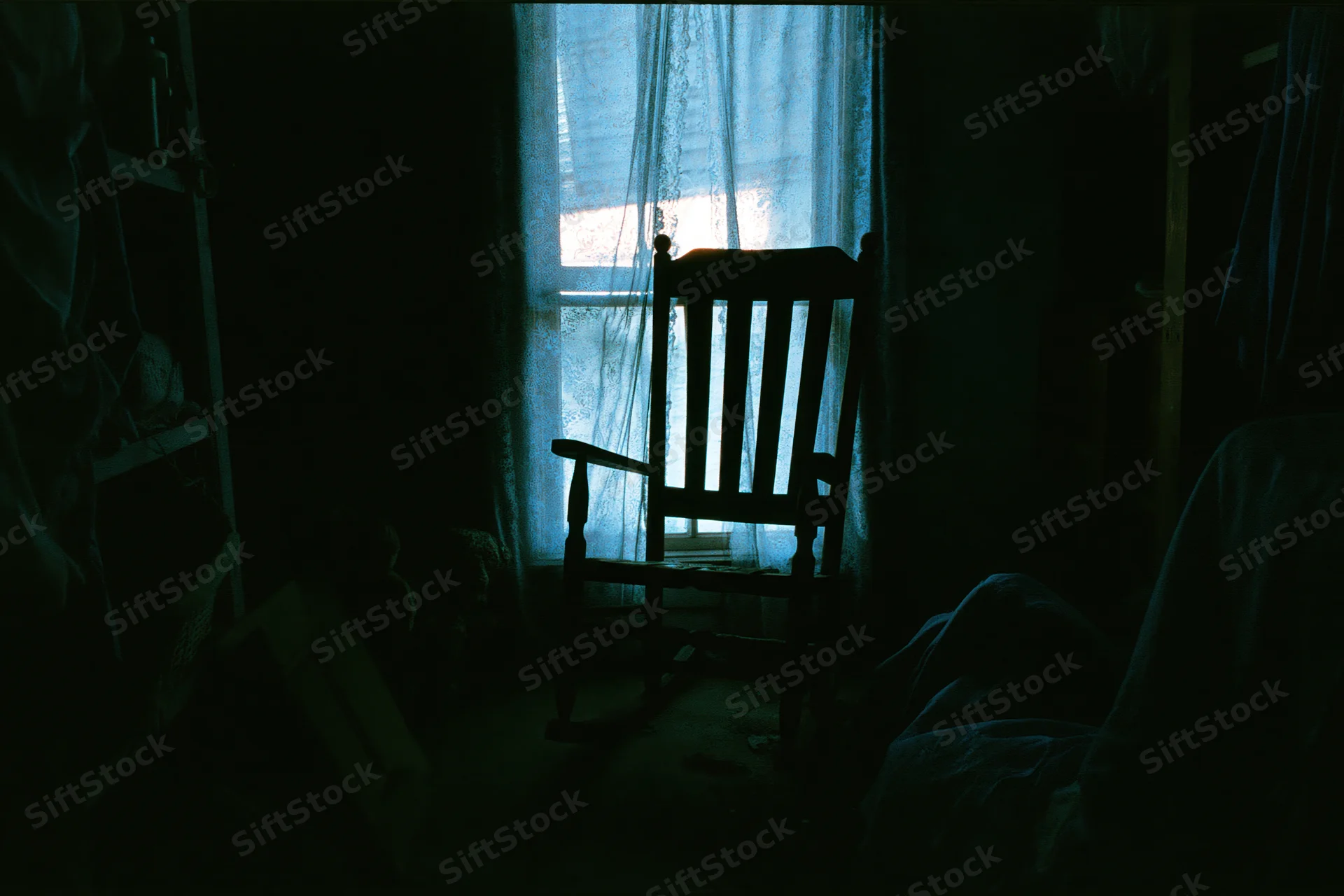 Wooden rocking chair silhouetted in a dark room by a curtained window