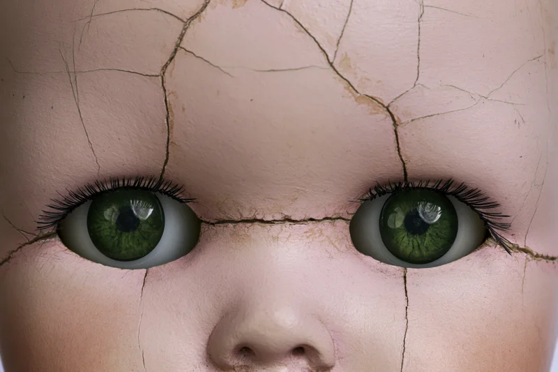 Close-up of cracked vintage porcelain doll face with green eyes