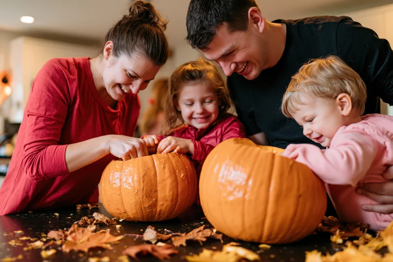 Family of four carving pumpkins together at kitchen table