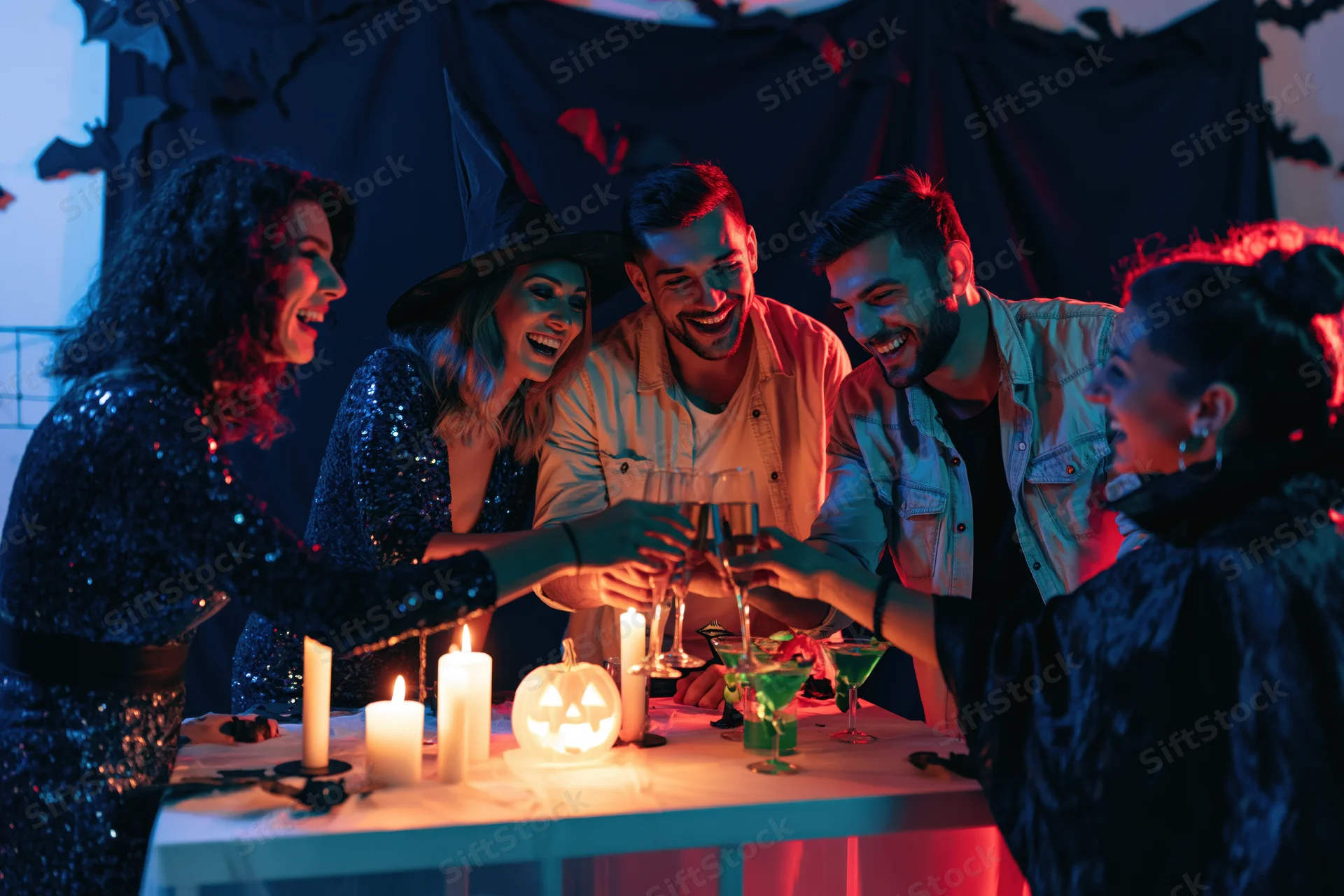 Five adults in halloween costumes clinking champagne glasses at a decorated table