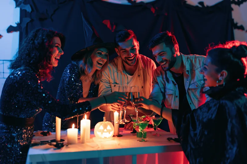 Five adults in halloween costumes clinking champagne glasses at a decorated table