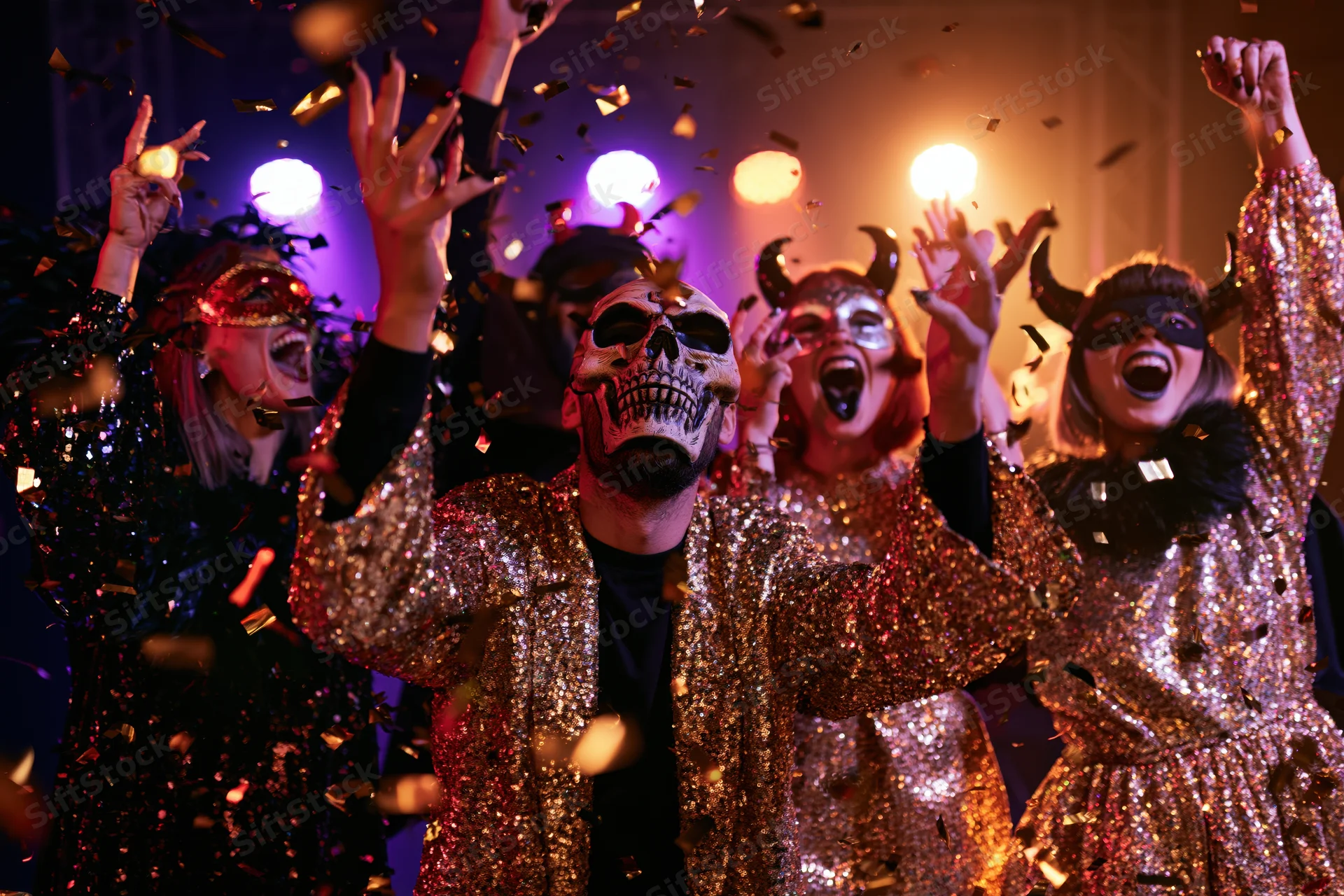 Adults in halloween costumes dancing with confetti under colorful lights at a party